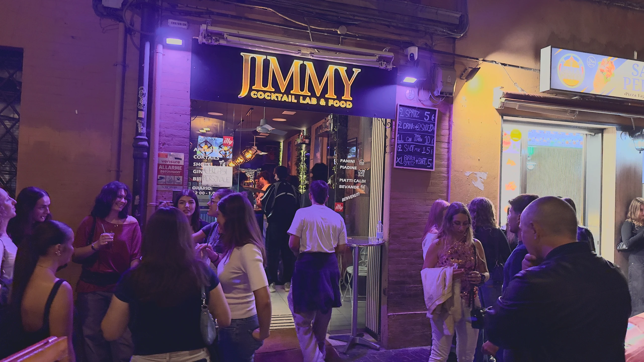 Persone davanti all'insegna illuminata di Jimmy in via Petroni.
